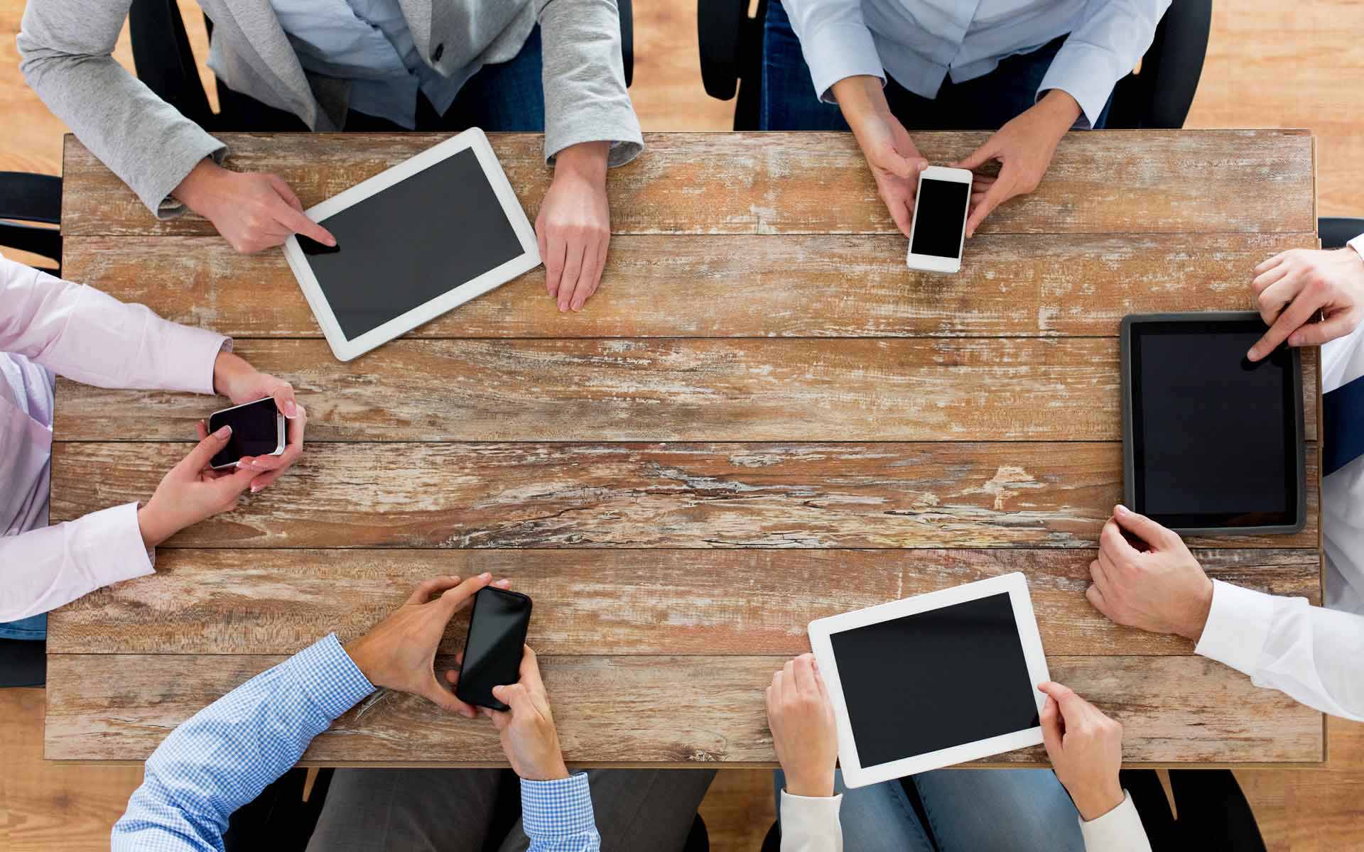 an image of a group around a rustic wooden table with phones and tablets